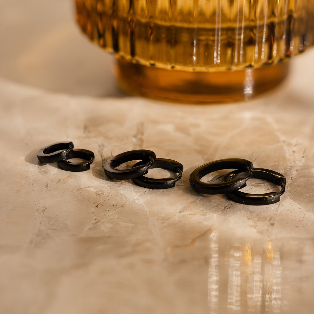 The Men's Black Hoops Set, displayed on a marble surface, makes a stylish choice for men's earrings or a perfect gift for him.