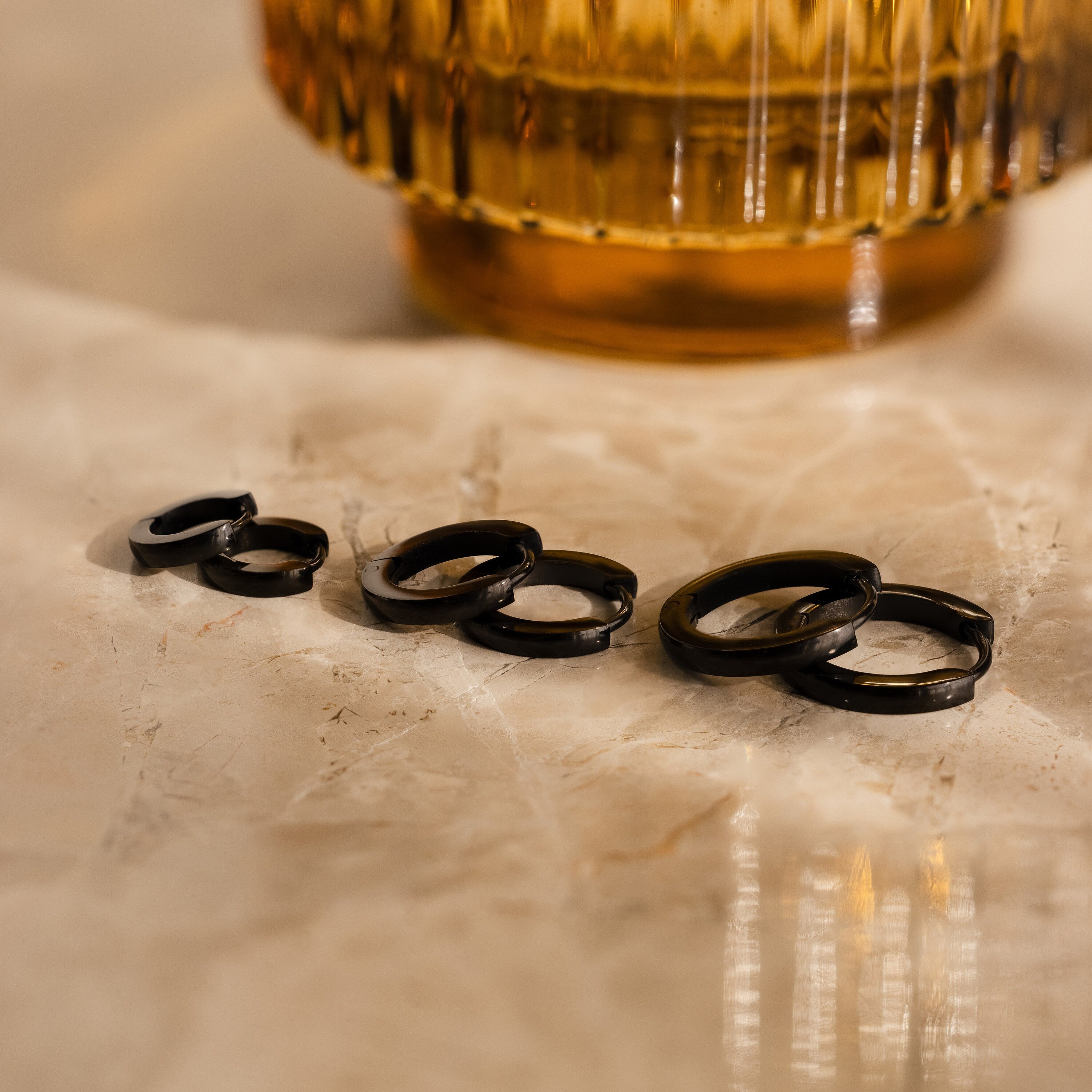 The Men's Black Hoops Set, displayed on a marble surface, makes a stylish choice for men's earrings or a perfect gift for him.