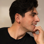 Man with dark hair and black shirt smiling, wearing the Men's Black Hoops Set—stylish earrings that make a perfect men's accessory and a thoughtful gift for him—looking to the right.