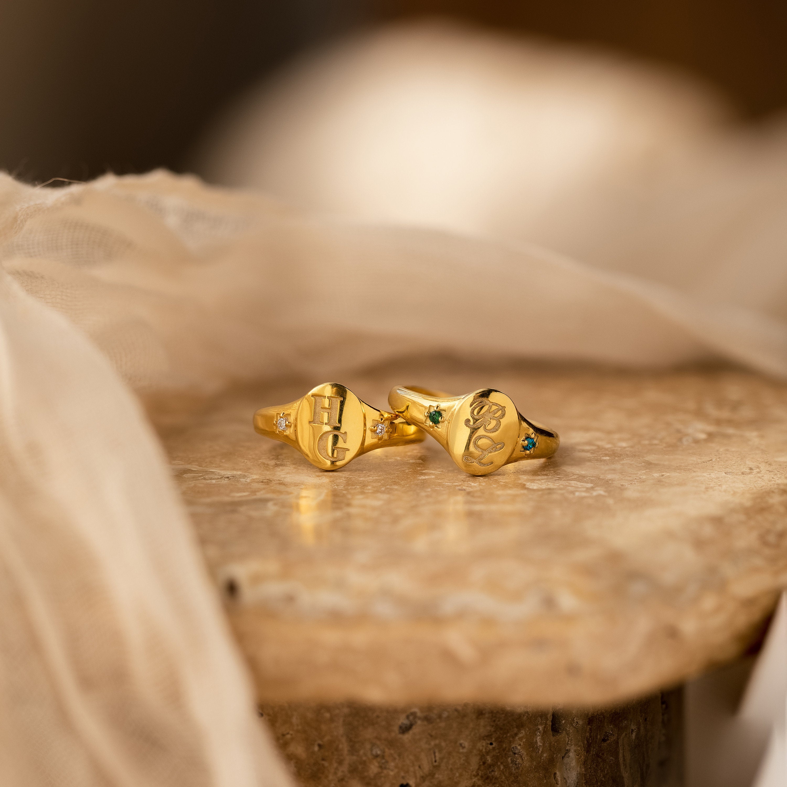 Two Initial Birthstone Signet Rings with engraved initials and gemstones are displayed on textured marble—a personalized jewelry piece and a unique custom gift.