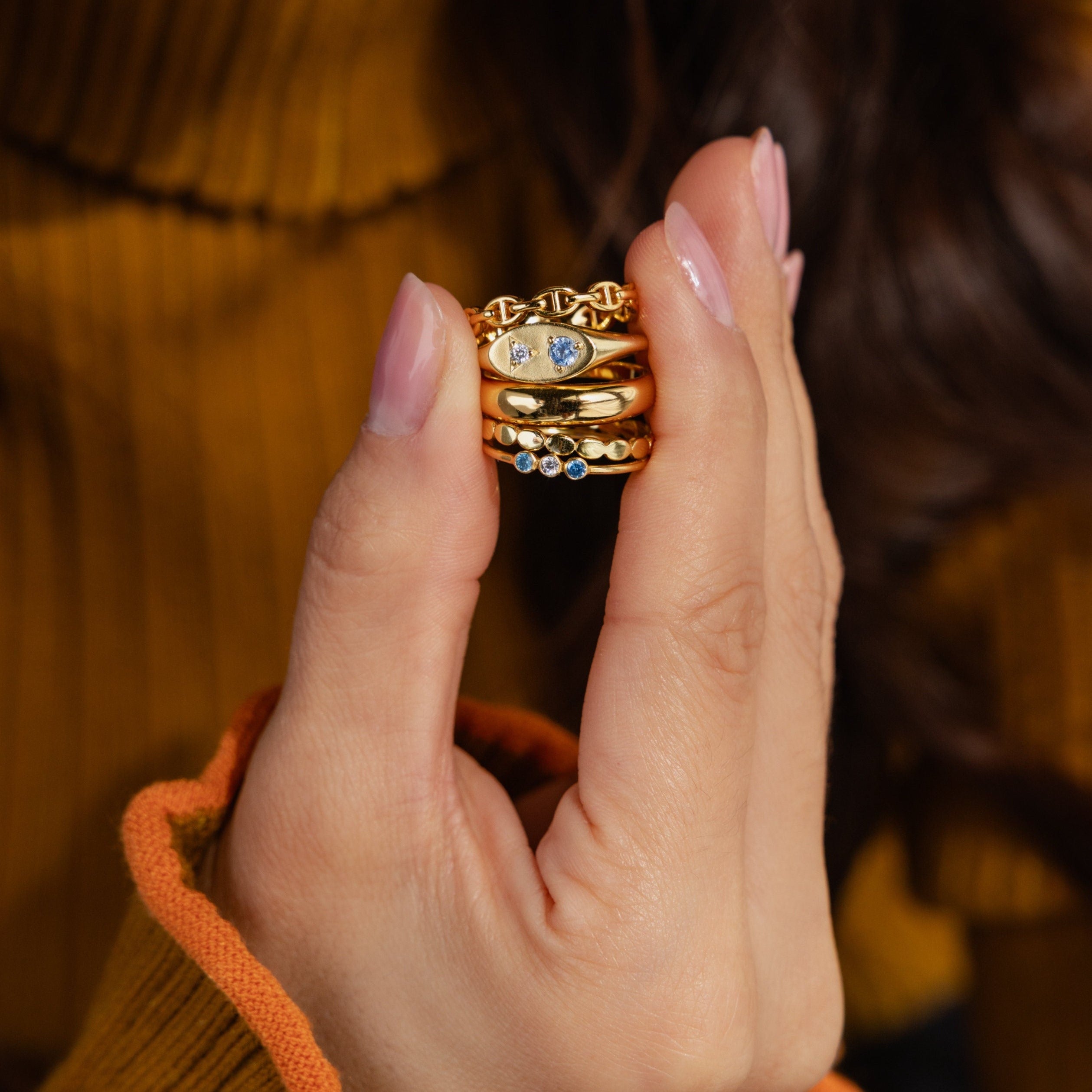 A manicured hand displays stacked gold rings, featuring the Mixed Birthstone Signet Ring for a personalized jewelry look with vibrant gemstones.