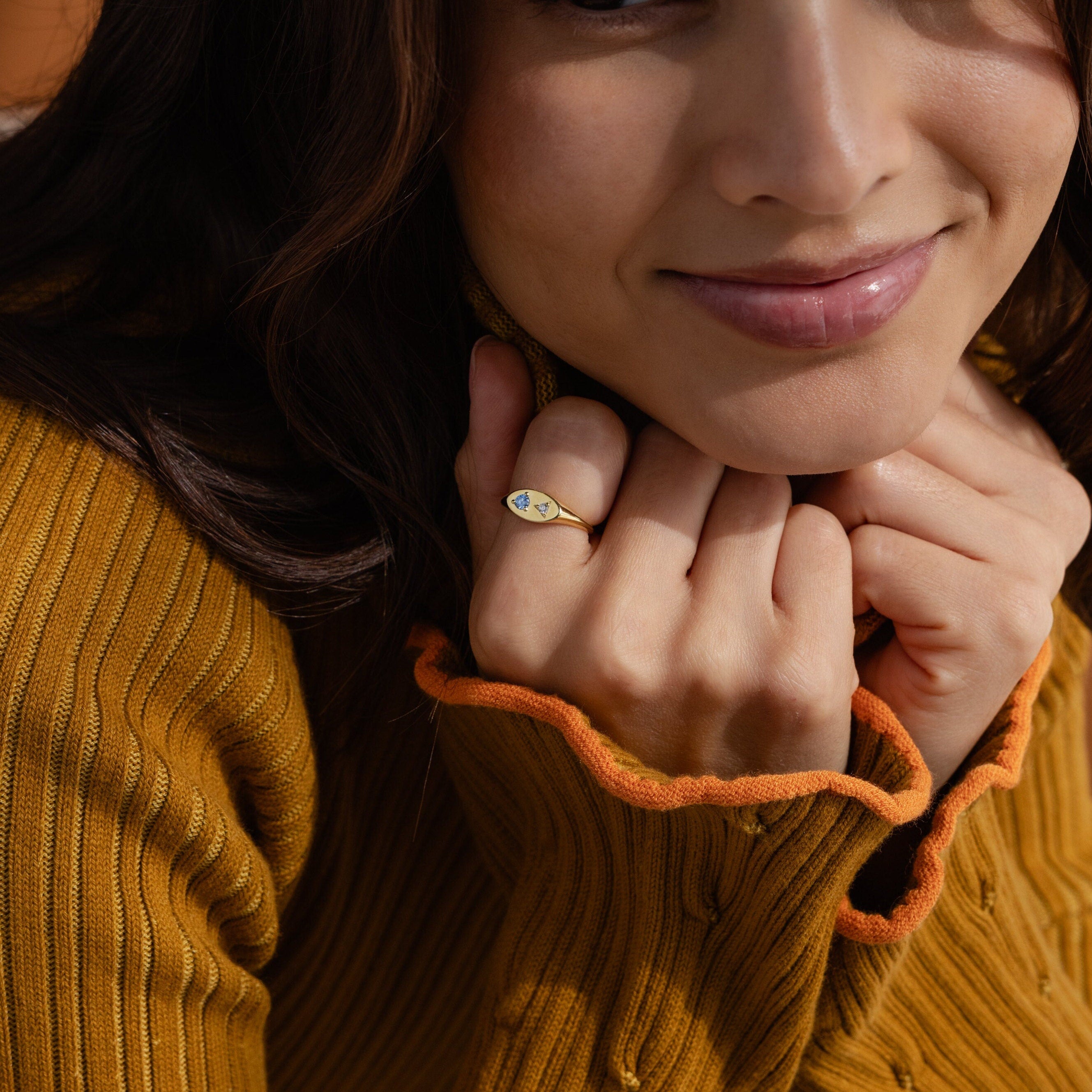 A woman in a mustard sweater smiles, holding her hands near her face and showing off the Mixed Birthstone Signet Ring.