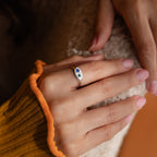 A hand with light pink nails wears the Mixed Birthstone Signet Ring, featuring blue and green accents, resting on a fuzzy surface for a unique statement look.