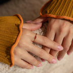 Close-up of hands wearing the Irregular Baguette Birthstone Ring with a red stone, styled with a mustard ribbed sweater.