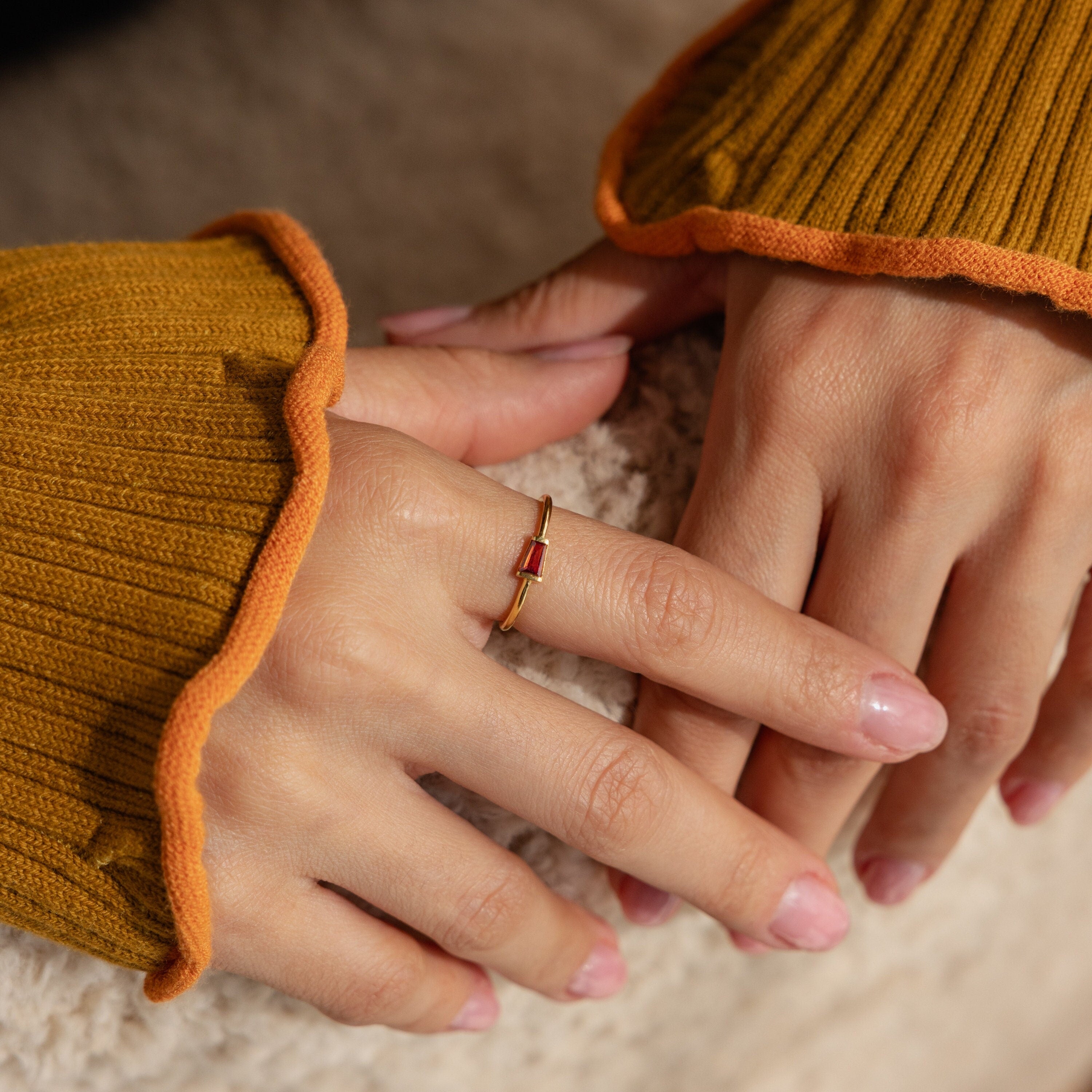 Close-up of hands wearing the Irregular Baguette Birthstone Ring with a red stone, styled with a mustard ribbed sweater.