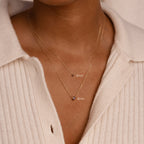 Two gold chain necklaces with small pendants, featuring a 4mm and 6mm Heart Birthstone Necklace, layered over a cream ribbed sweater—personalized jewelry that's perfect for a thoughtful birthday gift.