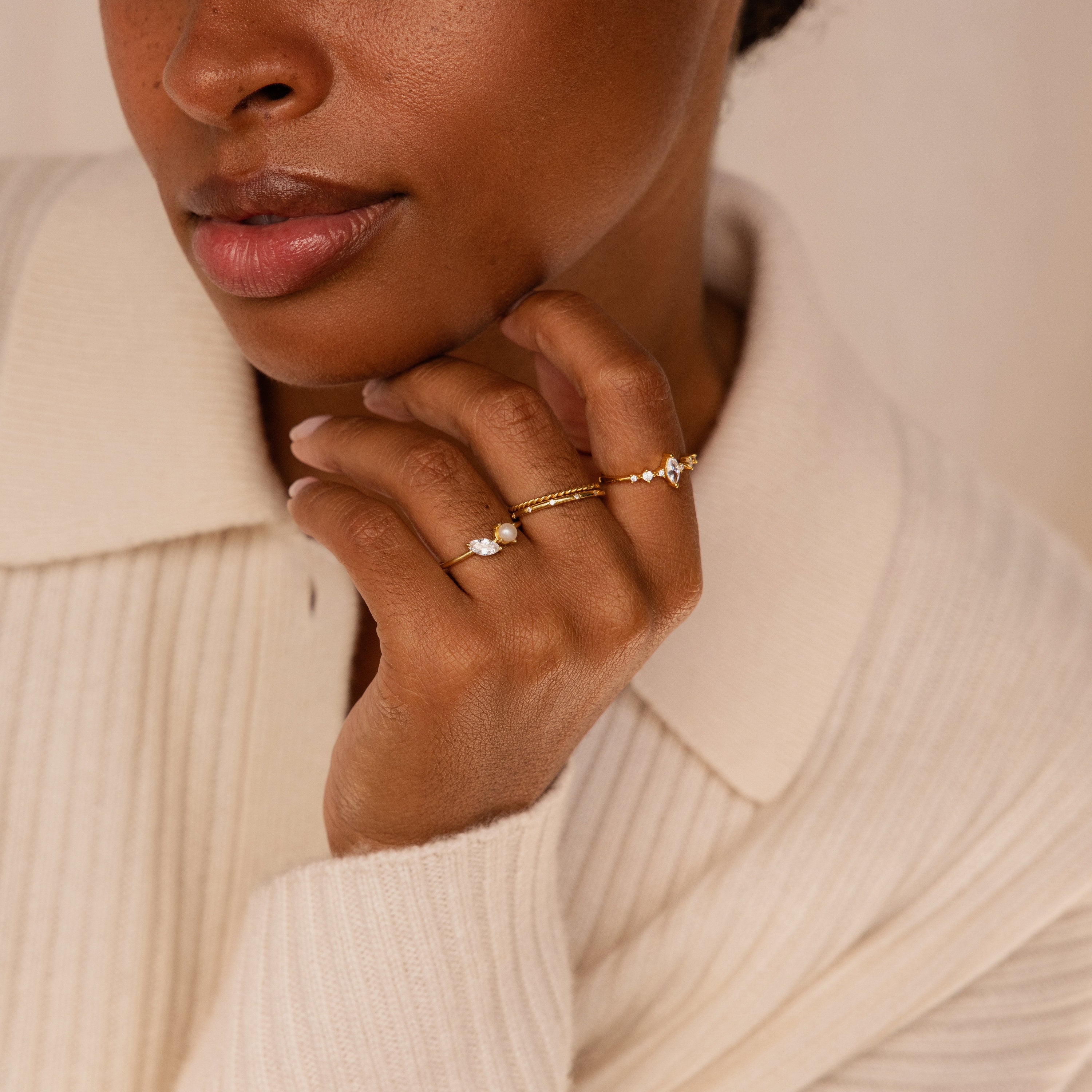 A woman in a cream sweater displays the Marquise Birthstone & Pearl Ring on her finger, held close to her face.