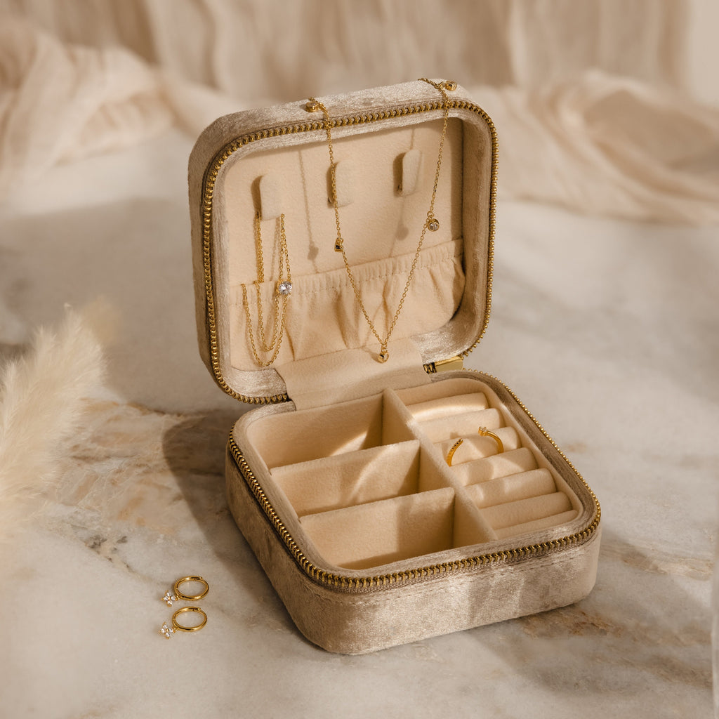 The Mystery Jewelry Box—a beige velvet case—displays hand-selected gold necklaces, rings, and earrings both inside and beside it.