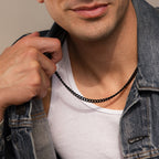 Man wearing a bold black Cuban link chain necklace styled with a white tank top and denim jacket for a modern streetwear look.