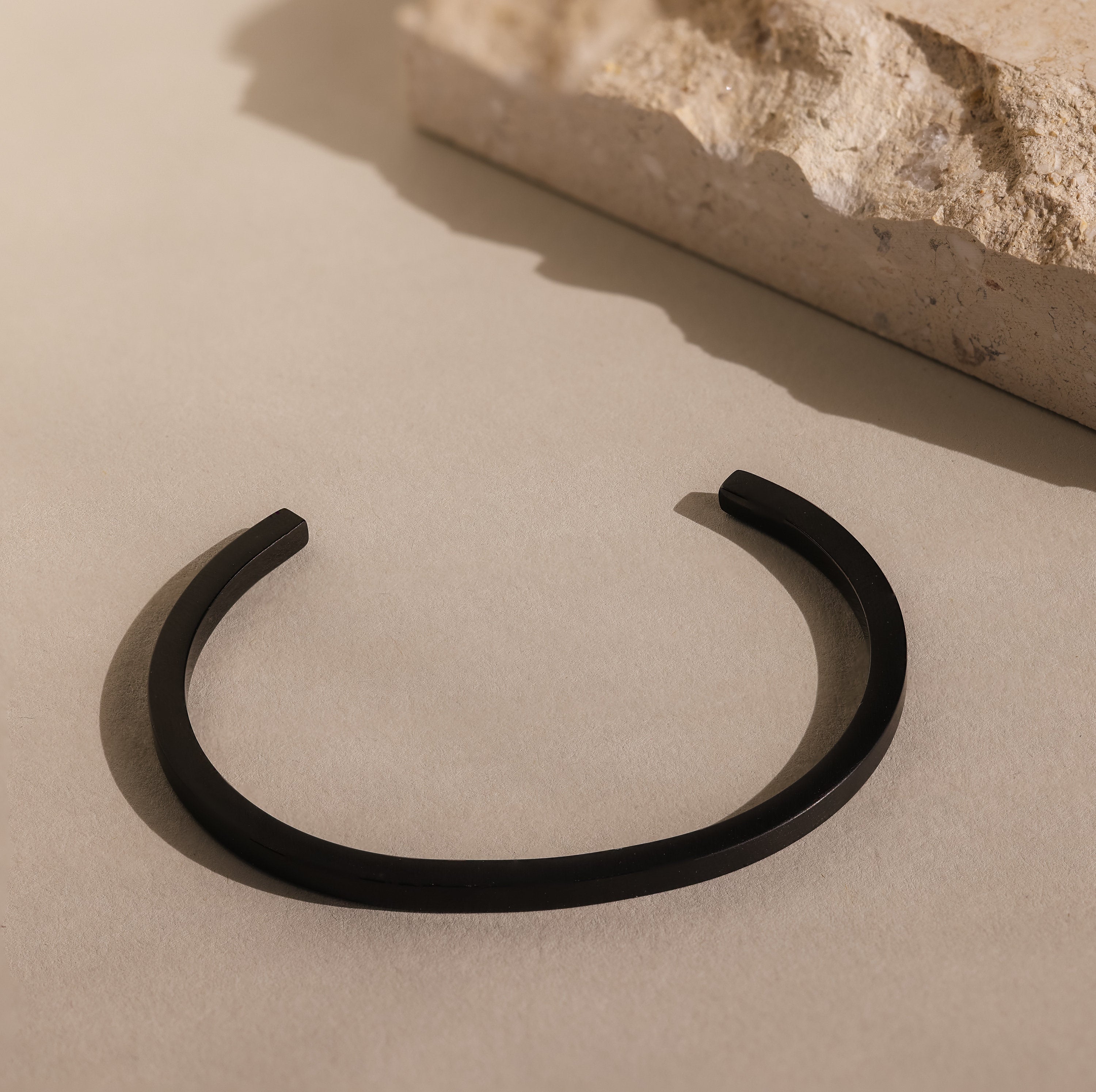 Men's Black Cuff Bracelet displayed on a beige surface beside a stone block—an ideal gift for him.