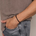 A man wears a Men's Black Cuff Bracelet, hand tucked into the pocket of faded blue jeans—a sleek and stylish gift for him.