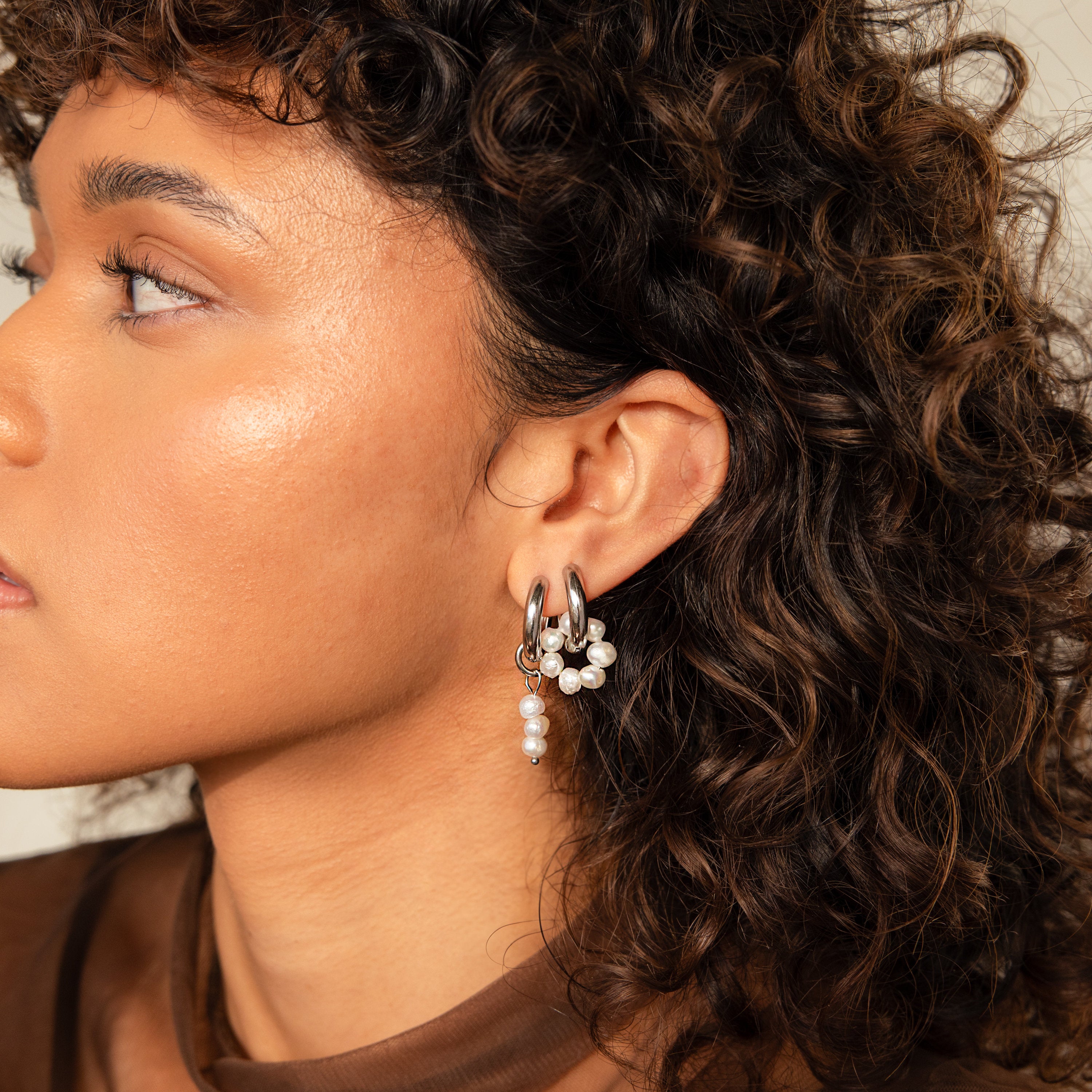 Woman with curly hair in profile wears Mismatched Pearl Drop Hoops—silver earrings with clustered and dangling pearls. A standout bridesmaid gift or a stylish pick for pearl earring lovers.