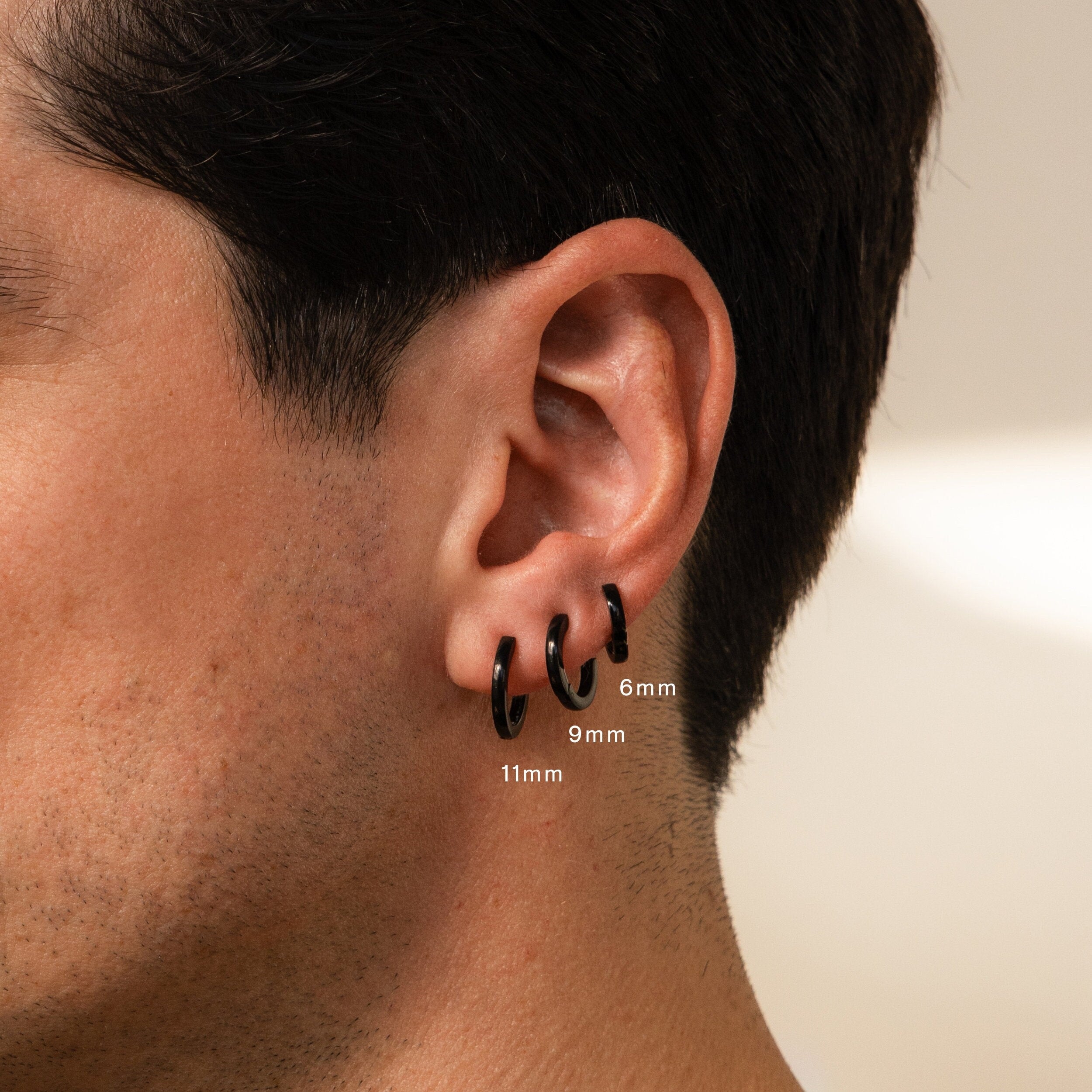 A close-up of a person's ear shows the Men's Black Hoops Set in 6mm, 9mm, and 11mm sizes—stylish earrings that make an ideal gift for him.