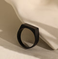 Men's Black Signet Ring with a matte geometric design, placed against a smooth, light surface with soft shadows.