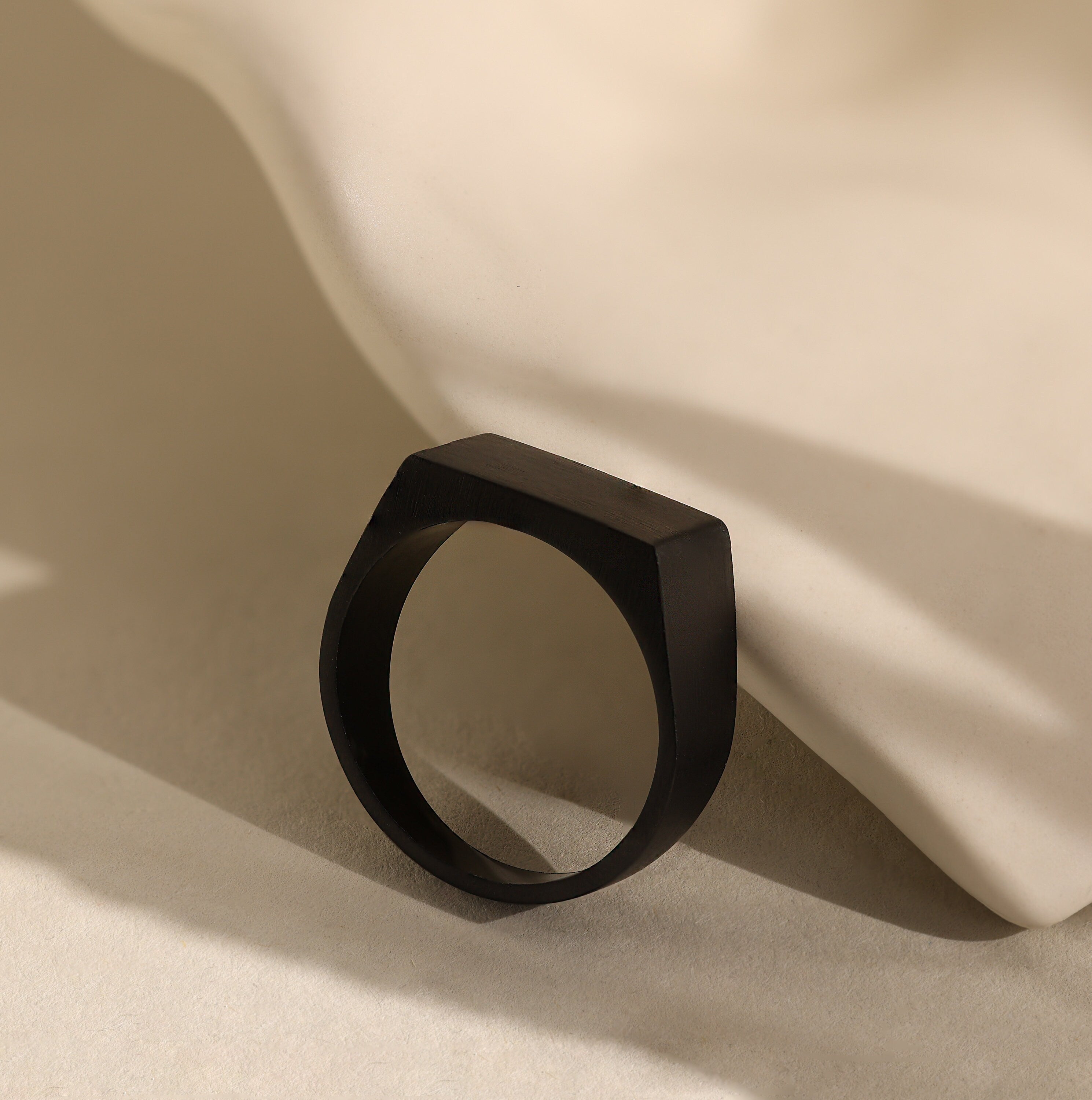 Men's Black Signet Ring with a matte geometric design, placed against a smooth, light surface with soft shadows.