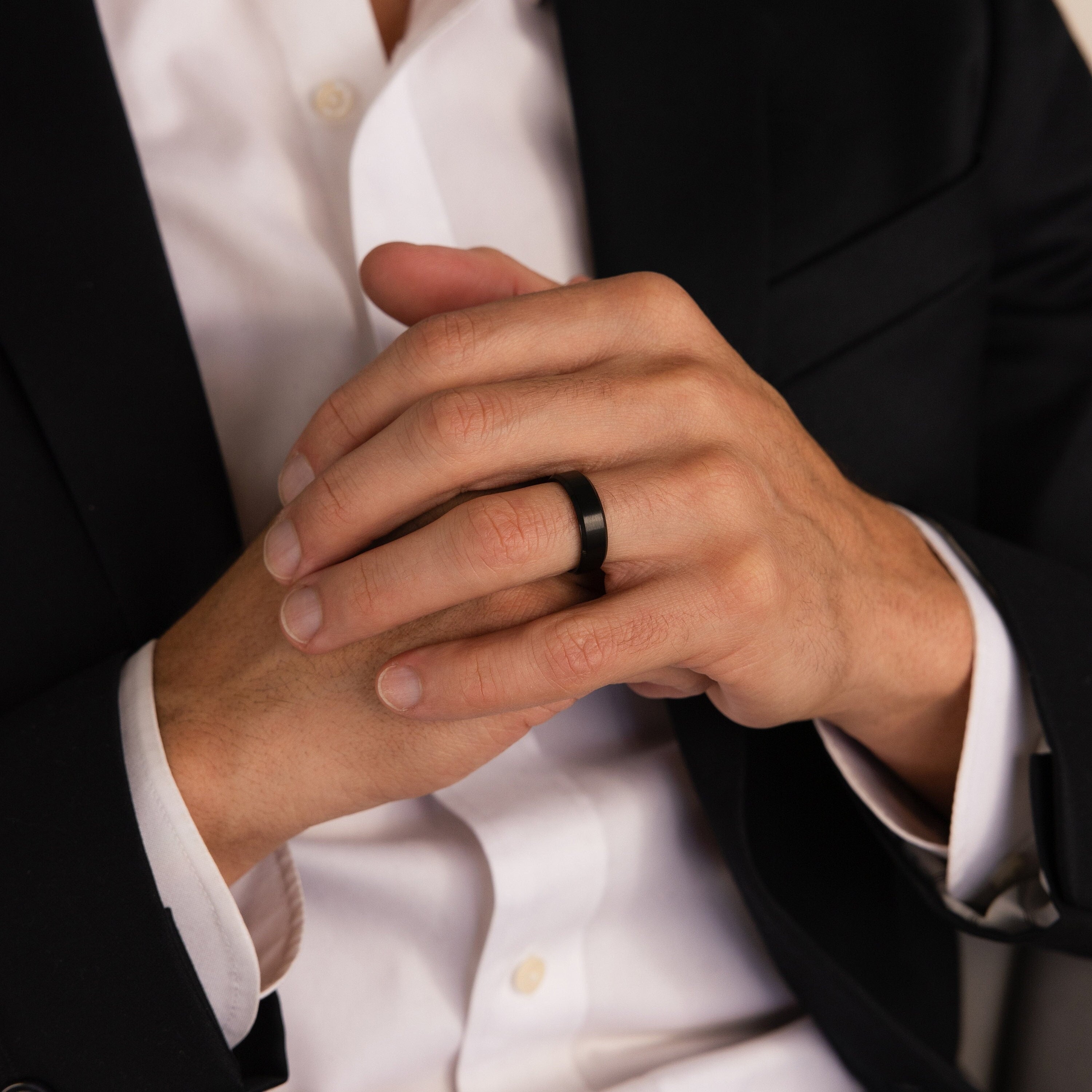 A person in a black suit wears the Men's Thick Black Ring, hands gently clasped together.