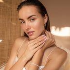A woman with slicked-back hair poses in a white top, wearing the elegant Triple Pearl Drop Earrings, softly illuminated by natural light.