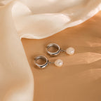 Pearl Drop Hoops with dangling pearls are displayed on a beige surface and draped in sheer cream fabric—an elegant, minimalist accessory for any occasion.
