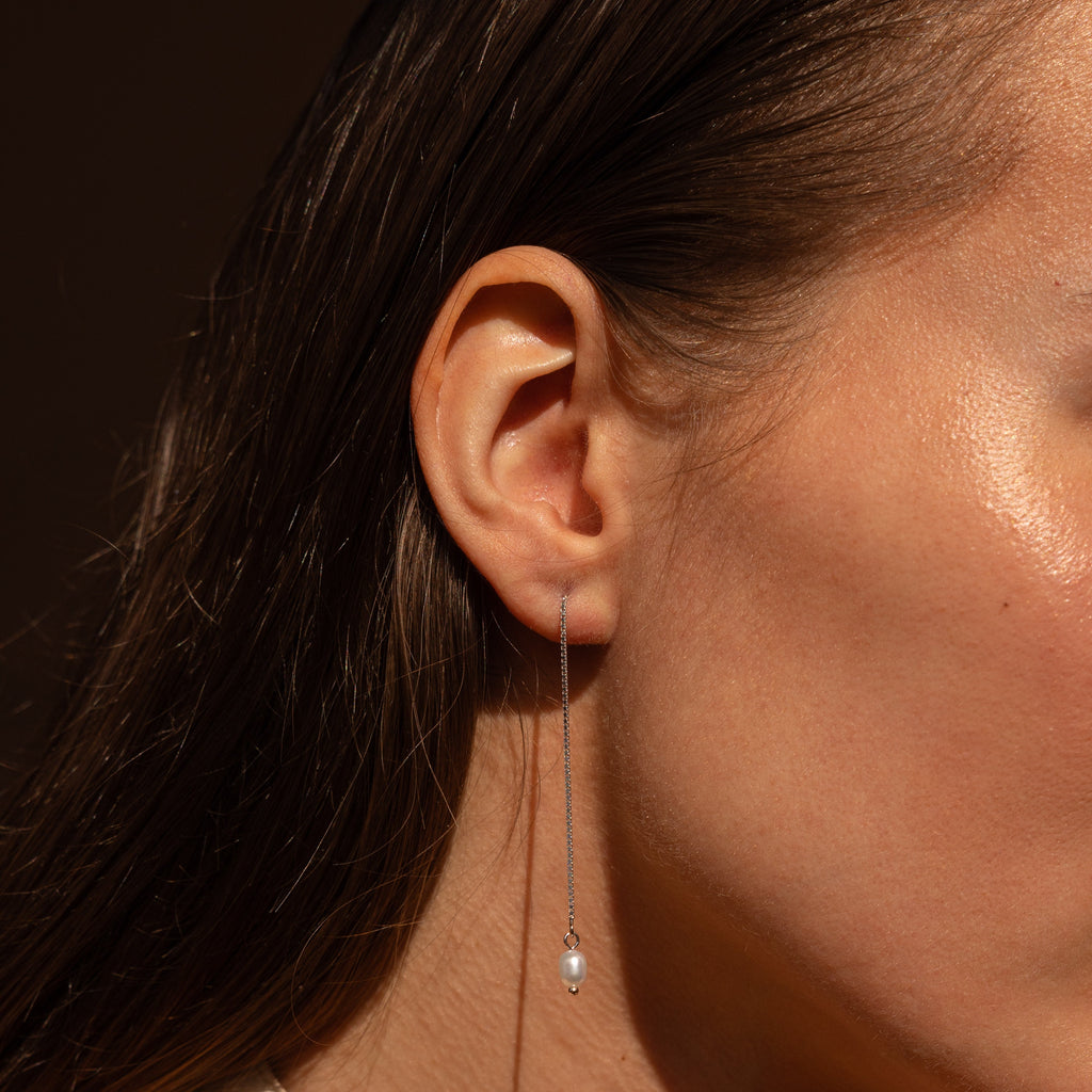 A close-up of a woman's ear wearing Pearl Threader Earrings, showcasing their minimalistic design with a delicate chain and a single pearl at the end.