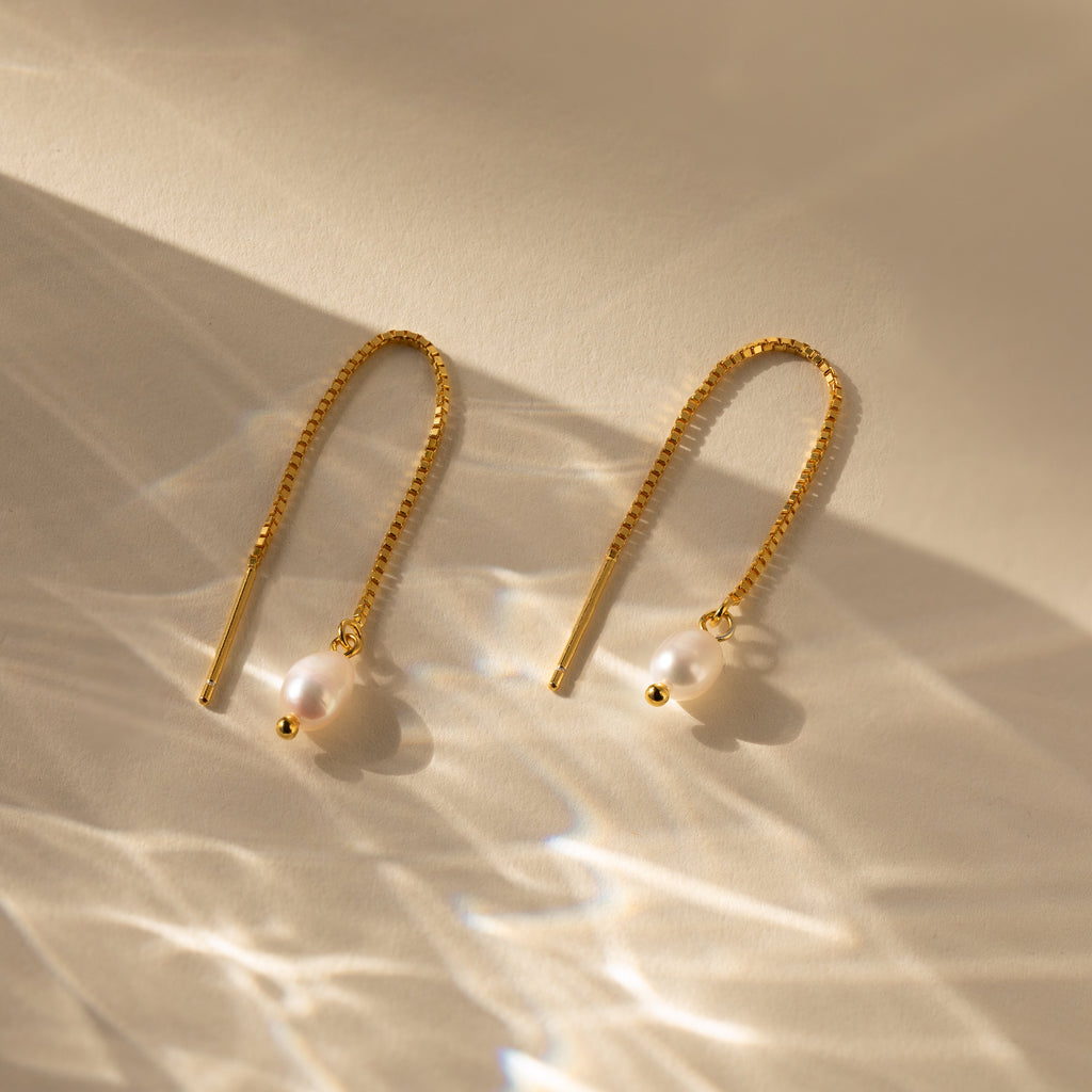 Pearl Threader Earrings are shown on a neutral background, their minimalistic gold design and pearls highlighted by soft, reflective lighting.