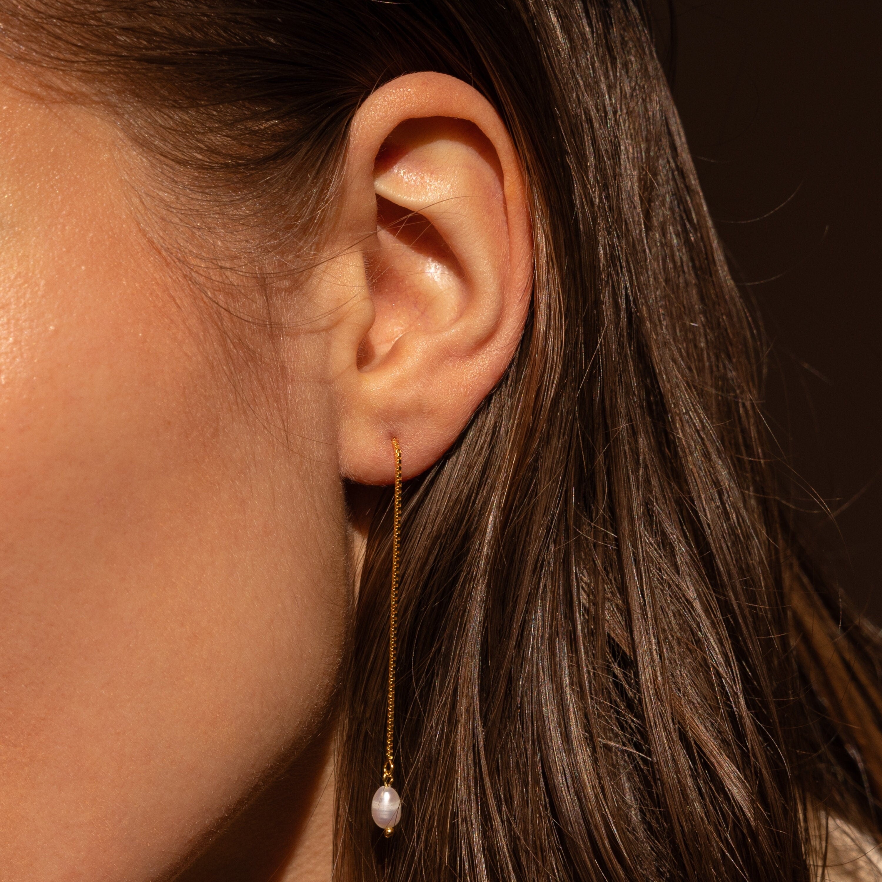 Close-up of a woman's ear wearing Pearl Threader Earrings, showcasing a long gold chain and a small pearl—ideal minimalistic dangle earrings for elegant style.