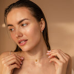 Woman with wet hair wears Dainty Knot Pearl Earrings, exuding timeless sophistication as she gazes to the side against a beige background.