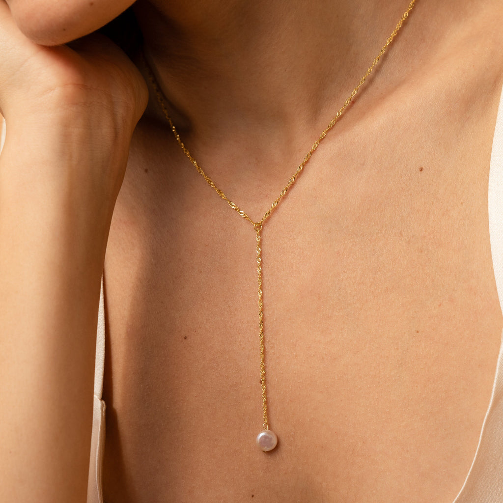 A woman wears a Pearl Lariat Y Necklace with a single pearl charm, shown close up on her neck and collarbone.
