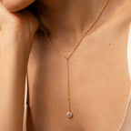 A woman wears a Pearl Lariat Y Necklace with a single pearl charm, shown close up on her neck and collarbone.