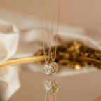 Two Pearl Hummingbird Necklaces, one silver and one gold with round pendants, are displayed on a reflective surface—ideal for those seeking a minimalist necklace with vintage-inspired charm.