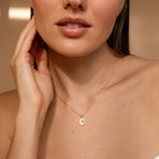 Close-up of a woman wearing the Pearl Hummingbird Necklace, gently touching her neck with one hand.