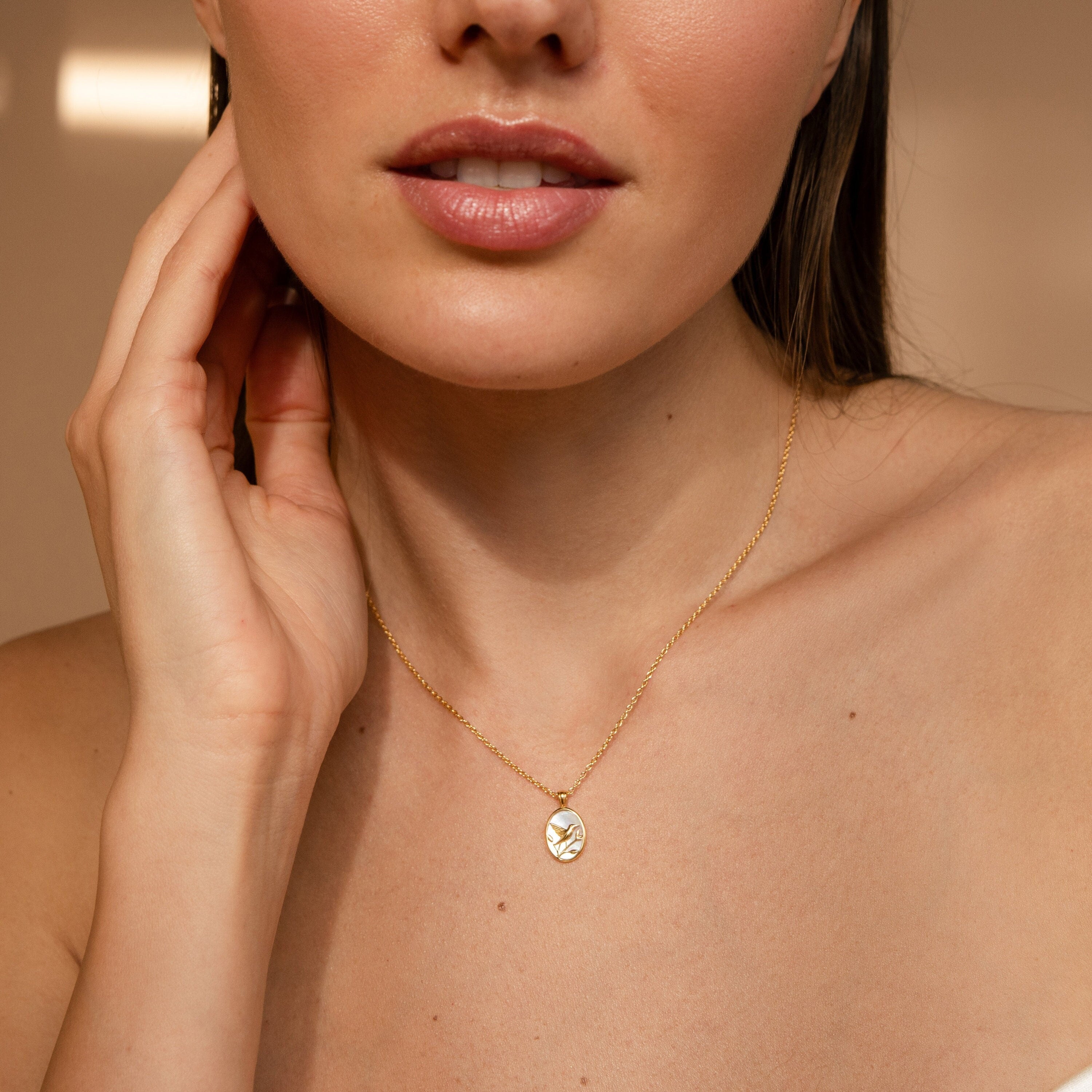 Close-up of a woman wearing the Pearl Hummingbird Necklace, gently touching her neck with one hand.