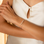 A woman in a white satin dress shows her arm, wearing the Duo Pearl Twist Bracelet—a delicate, minimalist piece adorned with pearls and silver.