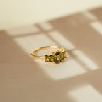 Art Deco Birthstone Ring—gold band with three baguette-cut green stones, displayed on a beige surface with soft shadows, radiating vintage charm.