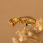 The Pave Oval Birthstone Ring, shown with sparkling gemstones and petite diamonds on a beige surface with dried flowers, is a stunning example of elegant gemstone ring design.