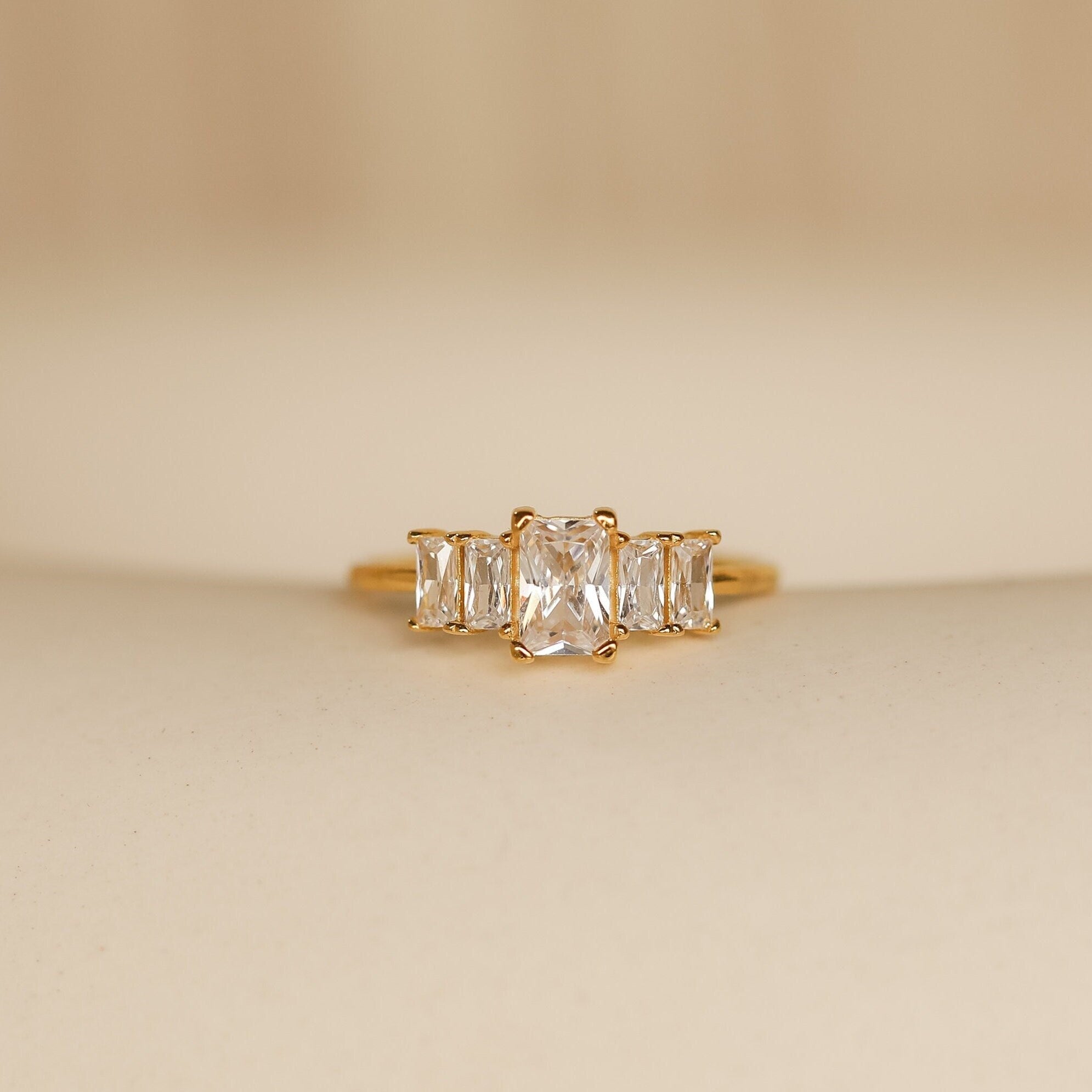 The Art Deco Birthstone Ring features a central rectangular diamond accented by baguette-cut stones on each side, exuding vintage elegance.