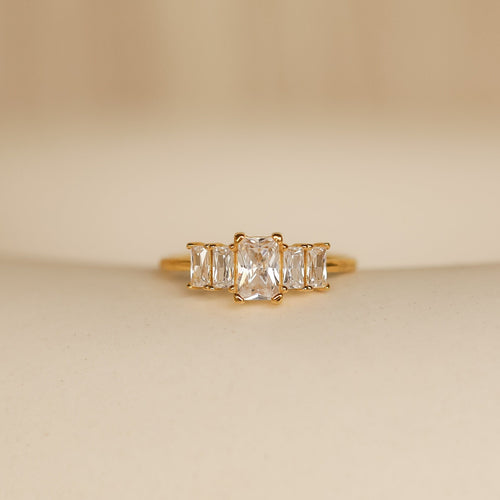 The Art Deco Birthstone Ring features a central rectangular diamond accented by baguette-cut stones on each side, exuding vintage elegance.