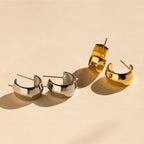 The Summer Statement Earrings Set includes two pairs of chunky twist hoops—one silver, one gold—displayed on a neutral beige surface. These stylish hoops are perfect summer accessories for effortless, standout looks.