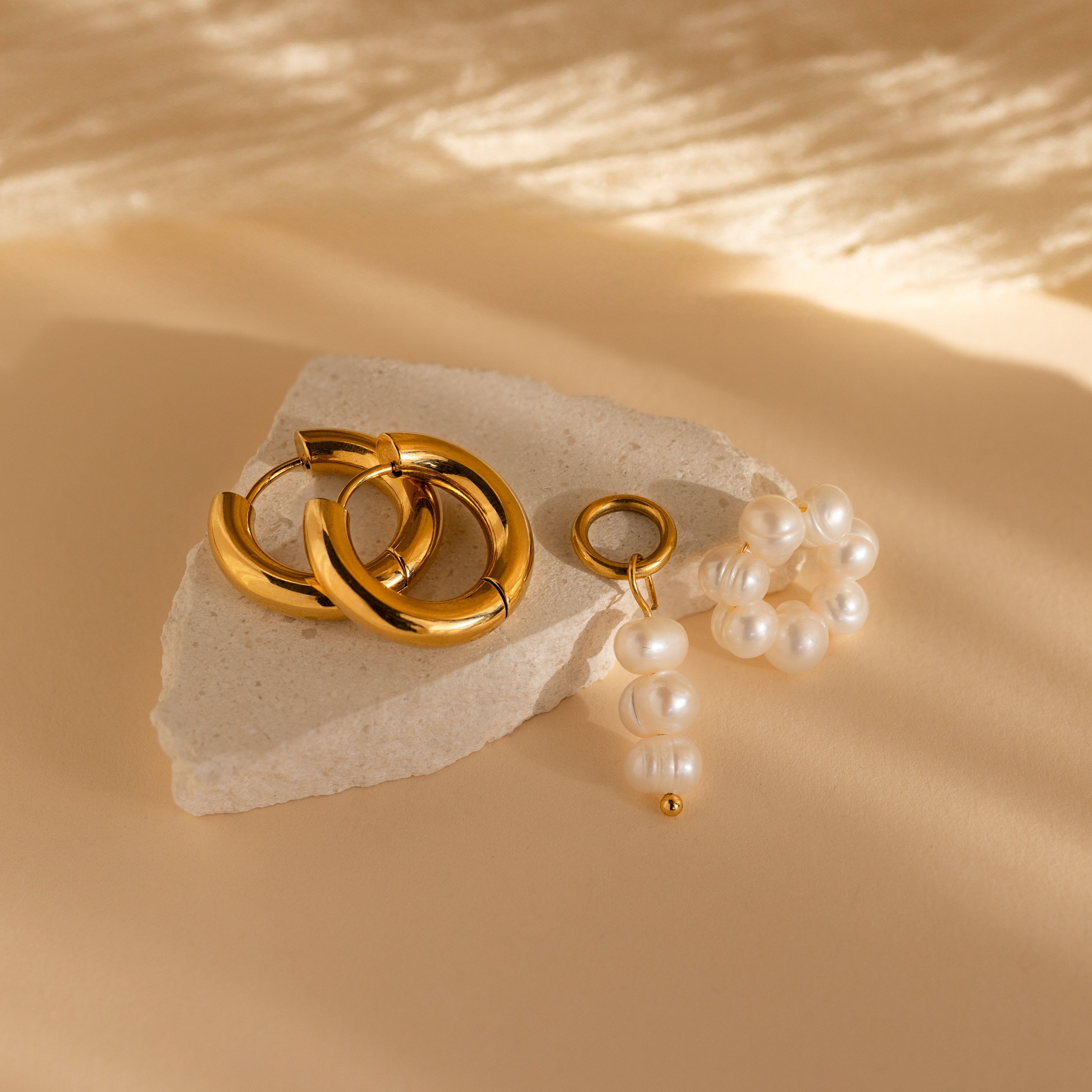 Mismatched Pearl Drop Hoops are displayed on white stone with a beige background.