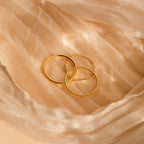 Three minimalist gold rings with unique textures rest on soft beige sheer fabric—a dainty Textured Stacking Ring Set ideal for effortless elegance.