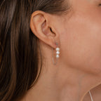 Close-up of a woman's ear wearing Triple Pearl Drop Earrings, showcasing three pearls in a silver setting with a delicate chain loop.