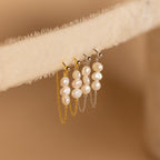 The Triple Pearl Drop Earrings feature elegant pearl drops with gold and silver chains, displayed gracefully on a soft beige surface—a stunning addition to your pearl jewelry collection.
