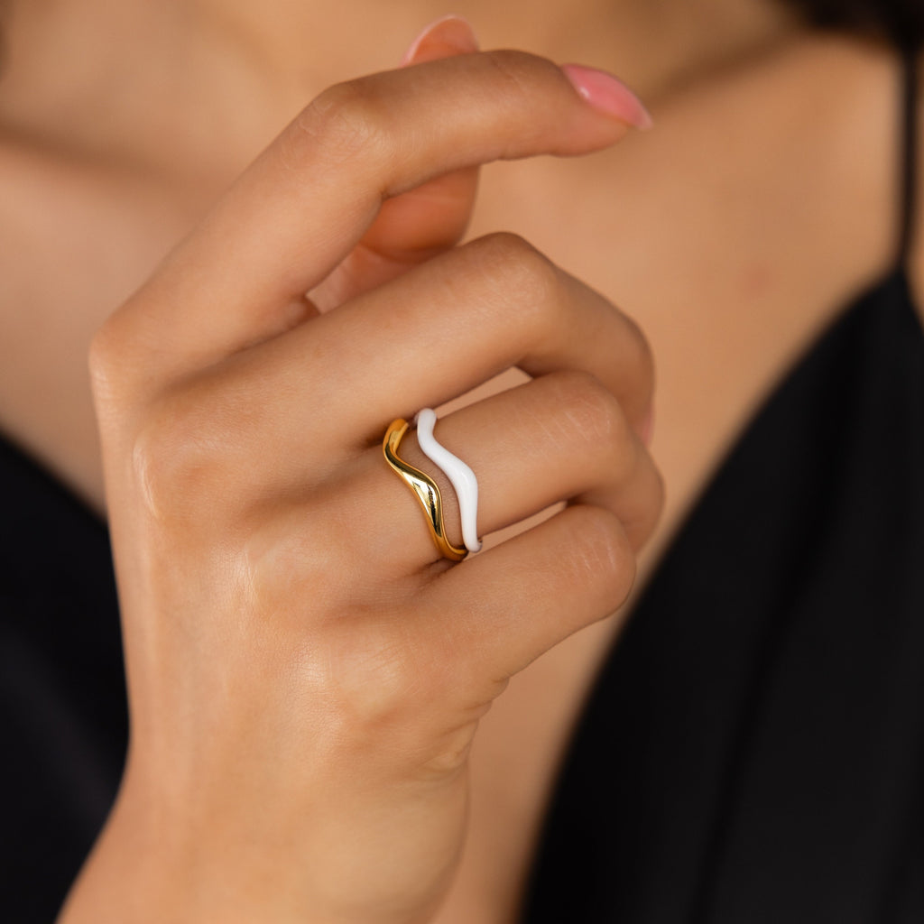 A hand with pink nails wears the Duo Wave Ring Set—gold and white minimalist rings with a unique wave design—shown against a black sleeveless top.