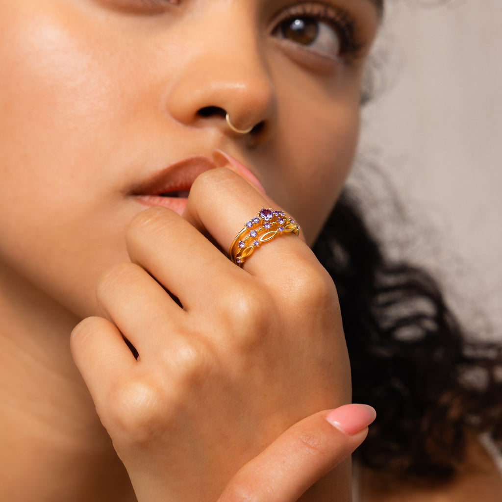 A woman wearing a gold nose ring and the Amethyst Stacking Ring Set touches her lips thoughtfully, highlighting fashion-forward jewelry.