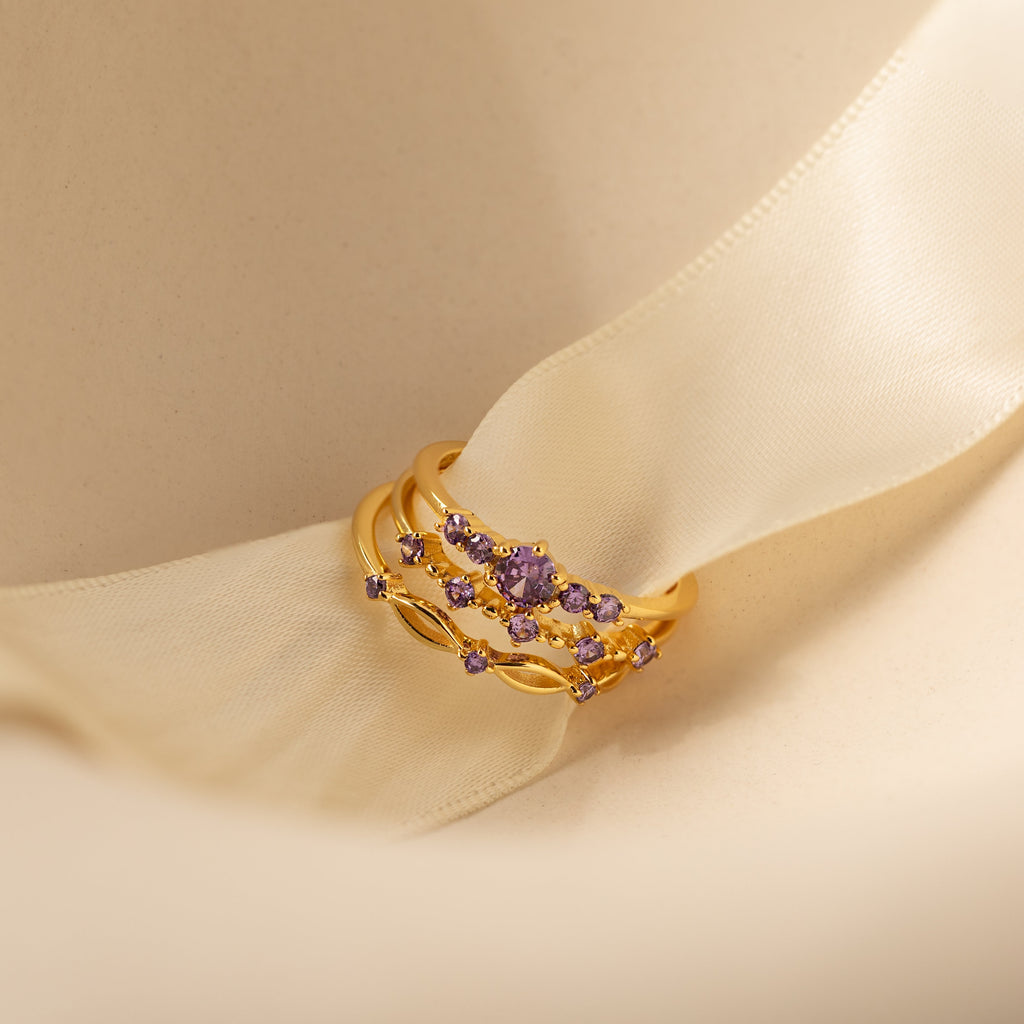 The Amethyst Stacking Ring Set features gold rings with purple gemstones on a cream satin ribbon, adding a bold, elegant touch to your style. This fashion-forward jewelry is perfect for stacking and making a statement.