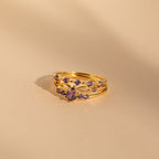 The Amethyst Stacking Ring Set features gold rings with purple gemstones in a delicate pattern on a beige background—ideal for stacking or wearing as a striking statement piece.