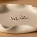 Three pairs of Pearl, Opal & Diamond Studs are displayed on a wavy beige ceramic dish.
