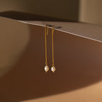 The Pearl Threader Earrings feature a minimalistic gold design with pearls delicately suspended from a chain, creating elegant dangling charm earrings.