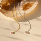 Two pearl necklaces—a gold dainty chain and the Pearl Lariat Y Necklace in silver—are displayed on a shell against a beige background.