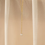 A delicate chain featuring a small round pendant is displayed on a beige, sheer fabric—perfect for fans of timeless elegance like the Pearl Lariat Y Necklace.