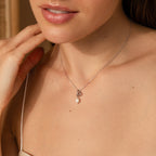 A woman in a beige top touches her neck while wearing the Dainty Knot Pearl Necklace, featuring a delicate pearl charm.